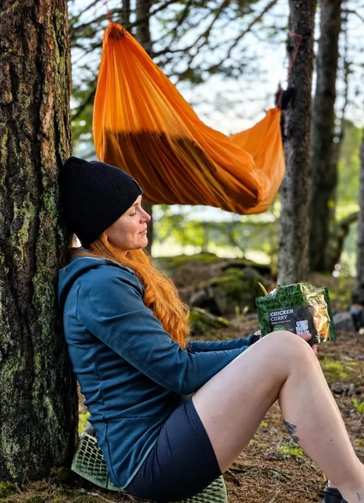 Hiker relaxing beside a hammock with a Good Mood Meals Chicken Curry pouch